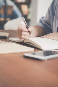 pexels-photo-733856-733856 A woman writes in a notebook at a café table with a coffee and smartphone nearby.